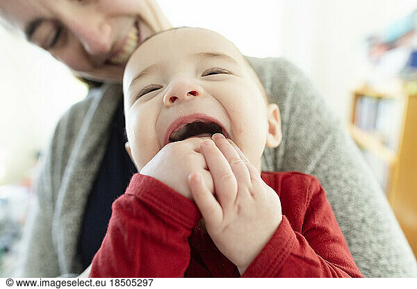 Baby Boy Smiling and Chewing on His Fingers While Being Held by Mom