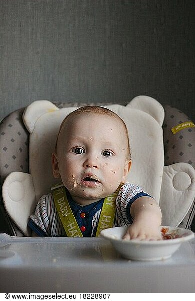 Baby boy with dirty face in feeding chair