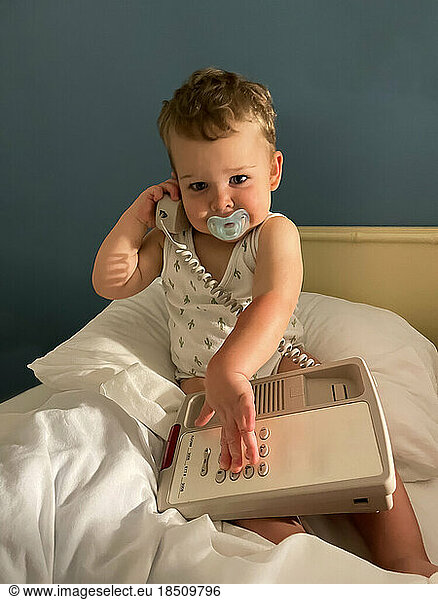 baby boy with pacifier and telephone on bed looking in to camera