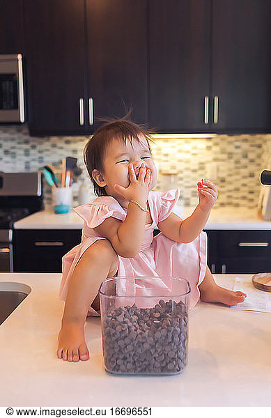 Baby daughter sitting on kitchen counter top eating chocolate chips.