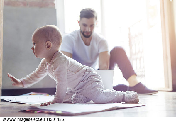 Baby girl crawling on floor near father working at laptop