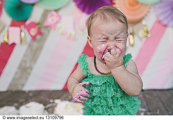 Baby girl crying while eating birthday cake during party