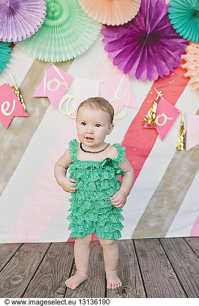 Baby girl looking away while standing against decoration at her first birthday party