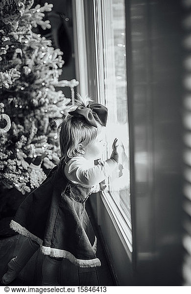 Baby girl looking out window next to Christmas tree