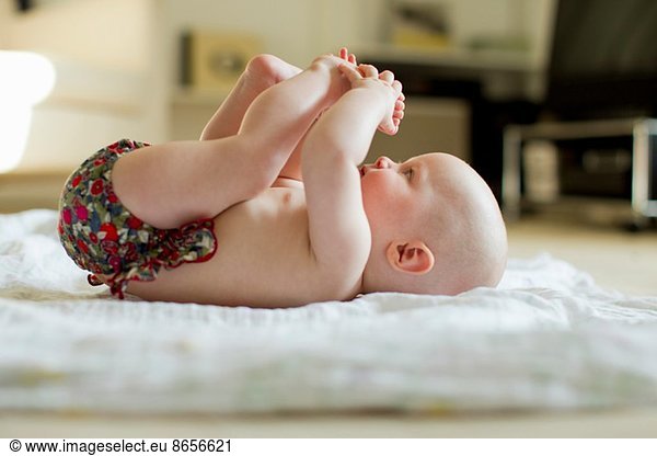 Baby girl lying on back playing with feet