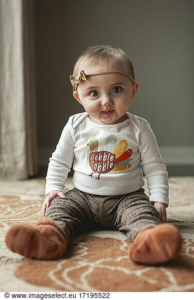 Baby girl 6-9 months sitting up in Thanksgiving outfit on rug at home