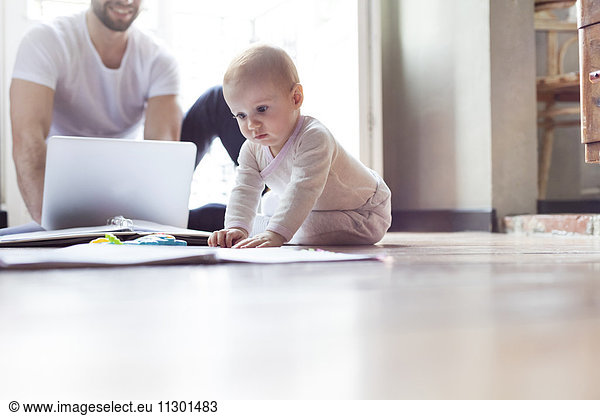 Baby girl playing on floor near father working at laptop