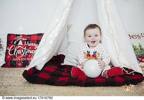 Baby girl playing with bauble while sitting in tent at home during Christmas
