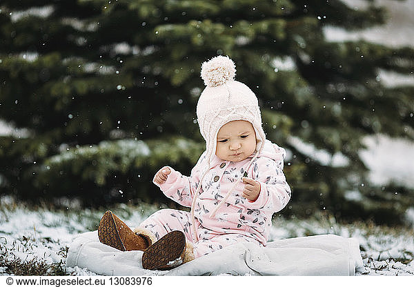 Baby girl sitting on blanket during snowfall