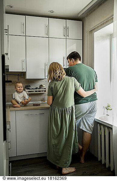 Baby girl sitting on counter by parents in kitchen