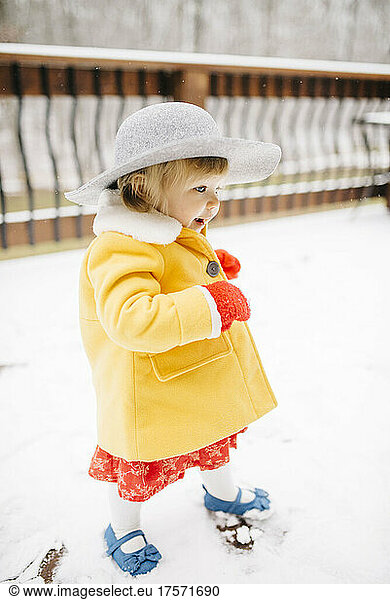 Baby girl walking in snow  wearing hat and yellow coat
