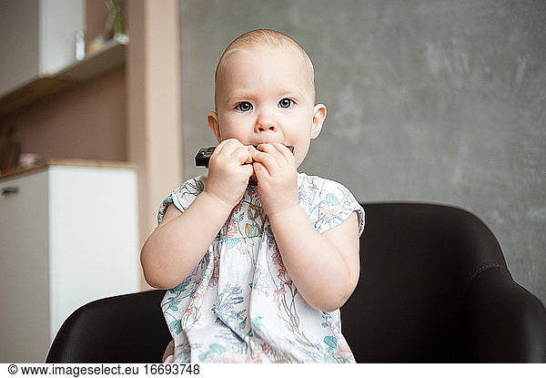 Baby girl with short hair close-up plays harmonica at home.