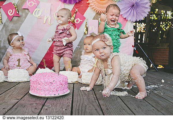 Baby girls with birthday cakes on floorboard