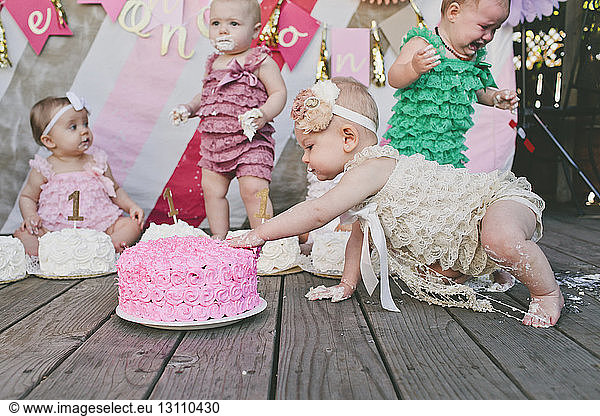 Baby girls with birthday cakes on floorboard at party