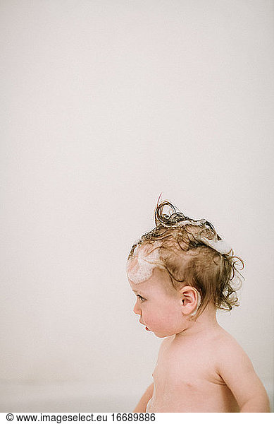 Baby in der Badewanne mit eingeseiften Haaren im Profil