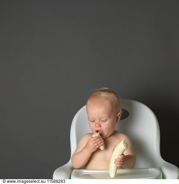 Baby in high chair eating a banana