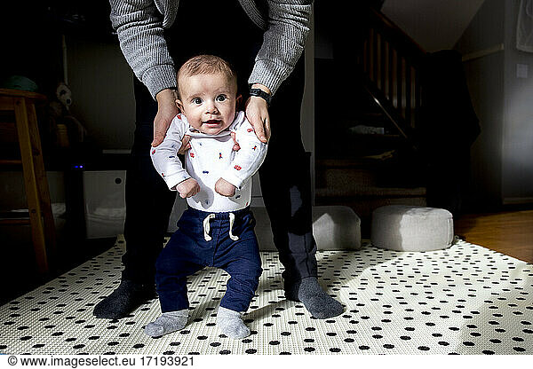 Baby standing on floor with support of mother while learning to walk