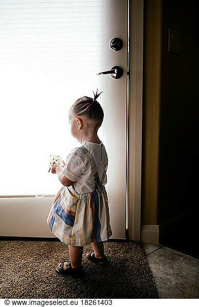 Baby wearing dress holding flowers by a bright window indoors