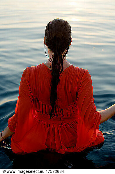 back of a woman in a wet red dress with long hair in blue water