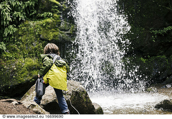 Back view child climbing and holding bag by waterfall