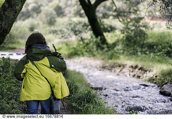 Back view kid hiking wearing green jacket by natural park