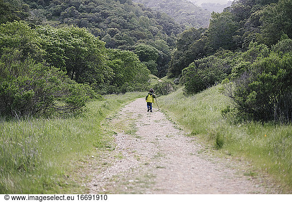 Back view kid hiking wearing raining coat in natural park