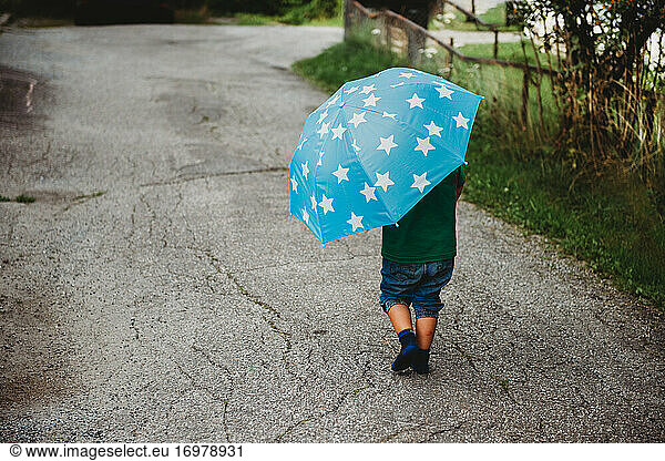 Back view of a child with an umbrella walking barefoot in the street