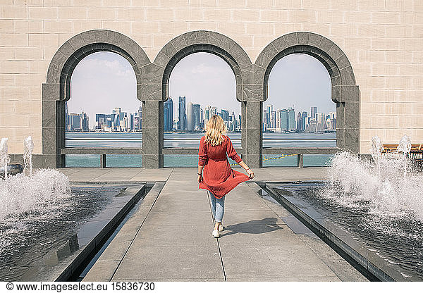 Back view of a woman walking between fountains and holding her dress