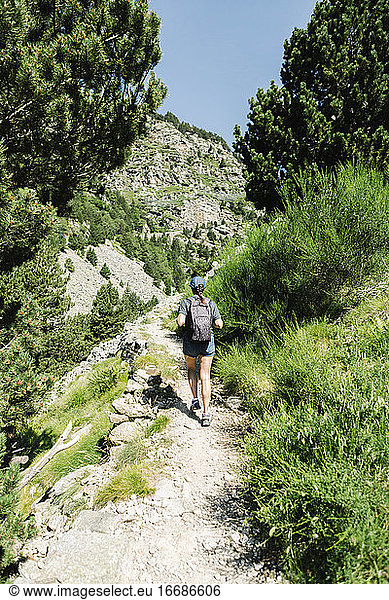 Back view of adventure female hiker in casual clothes walking along a mountain path in a sunny day