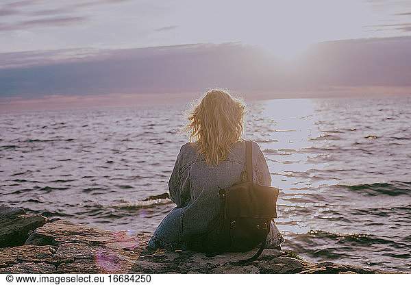 Back view of blond woman sitting by the sea at sunset