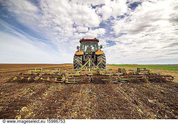 Back view of farmer in tractor plowing field in spring