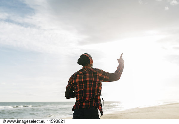 Back view of man walking on the beach listening music with headphones