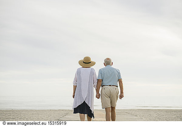 Back view of senior couple standing hand in hand on wooden boardwalk looking to the sea, Liepaja, Latvia, Back view of senior couple standing hand in hand on wooden boardwalk looking to the sea, Liepaja, Latvia