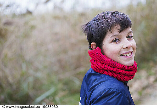 Back view of smiling teen wearing a red scarf while looking back to camera outdoors in nature