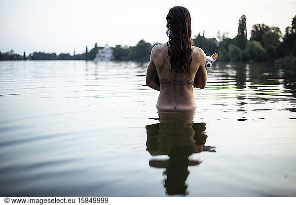 back view of strong woman holding small dog in natural berlin lake