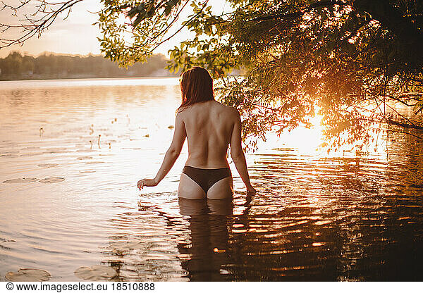 Back view of topless sensual woman standing in water at sunset