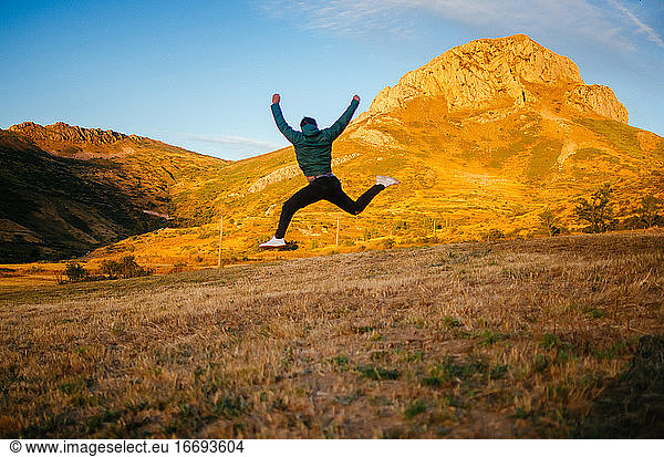 back view of unrecognizable male in casual clothes jumping high against mountains