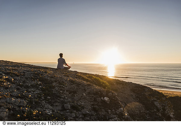 Back view of woman meditating on cliff at sunset