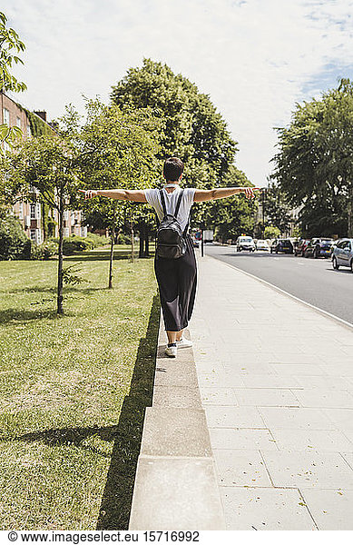 Back view of woman with backpack balancing on a wall