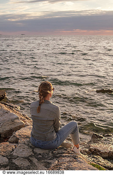 Back view of young woman sitting and looking at the sea