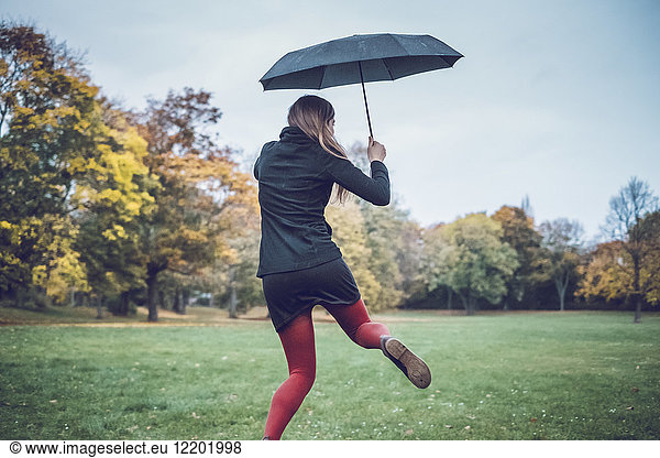 Back view of young woman with umbrella dancing in autumnal park
