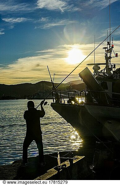 Backlight shot of silhouette of angler casting fishing rod in harbour just in front of sunset  Portoferraio  Elba  Tuscany  Italy  Europe