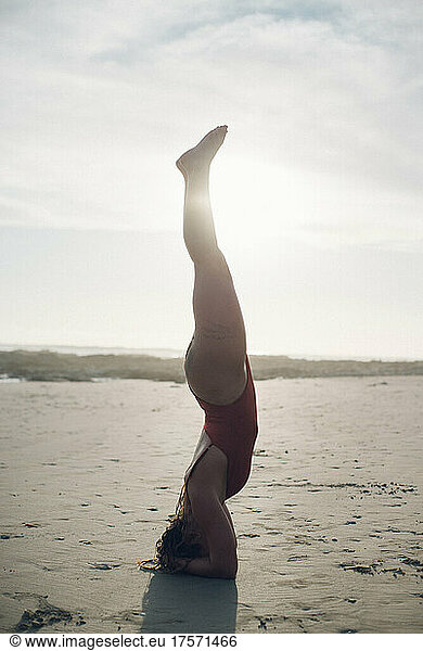 backlighting portrait of a blond girl making a yoga pose on the beach