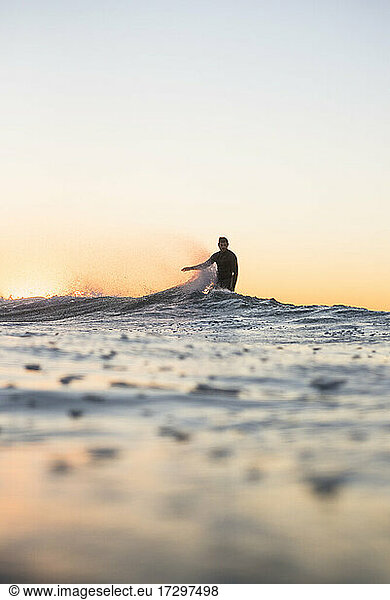 Backlit Man Surfing a wave during summer sunset