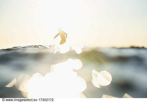 Backlit Man Surfing a wave during summer sunset