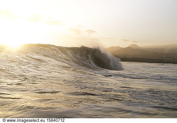 Backlit scene of wave breaking at sunset with shoreline in background