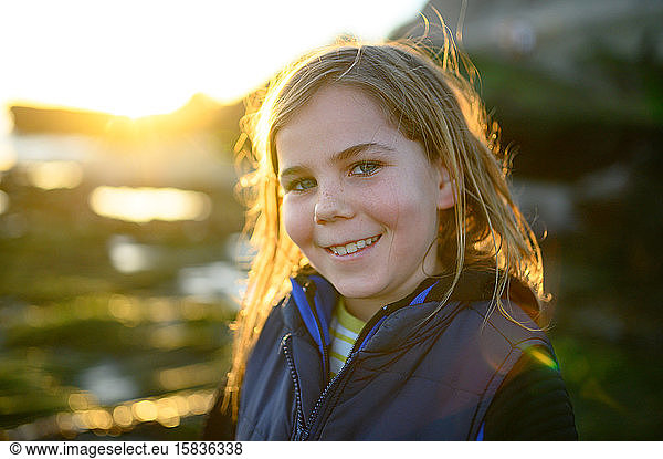 Backlit sunset portrait of long haired boy smiling at the camera