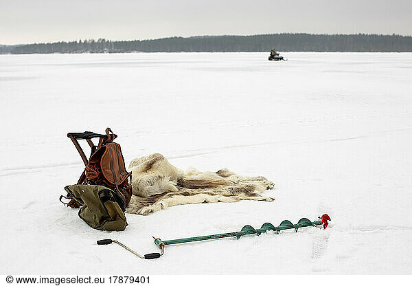 Backpack kept by animal skin and ice auger on snow in winter