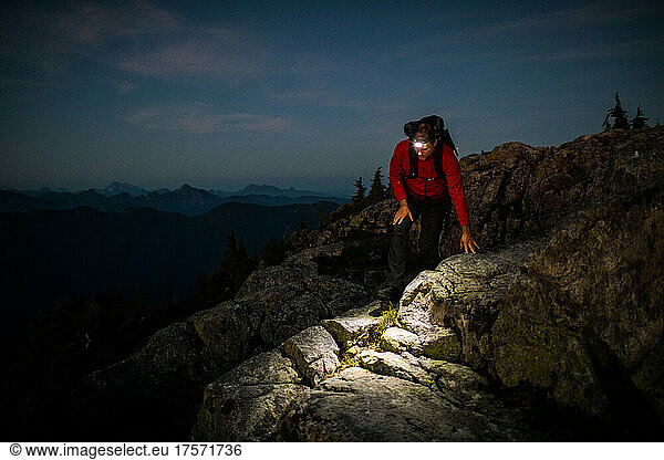 Backpacker carefully hikes rocky summit at night with headlamp