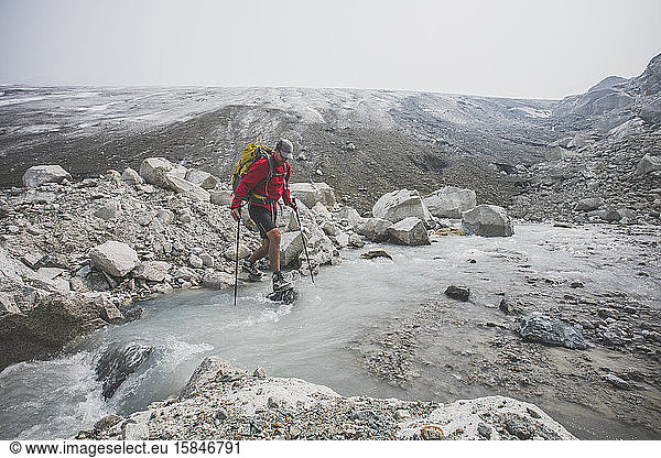 Backpacker crosses stream below melting glacier.